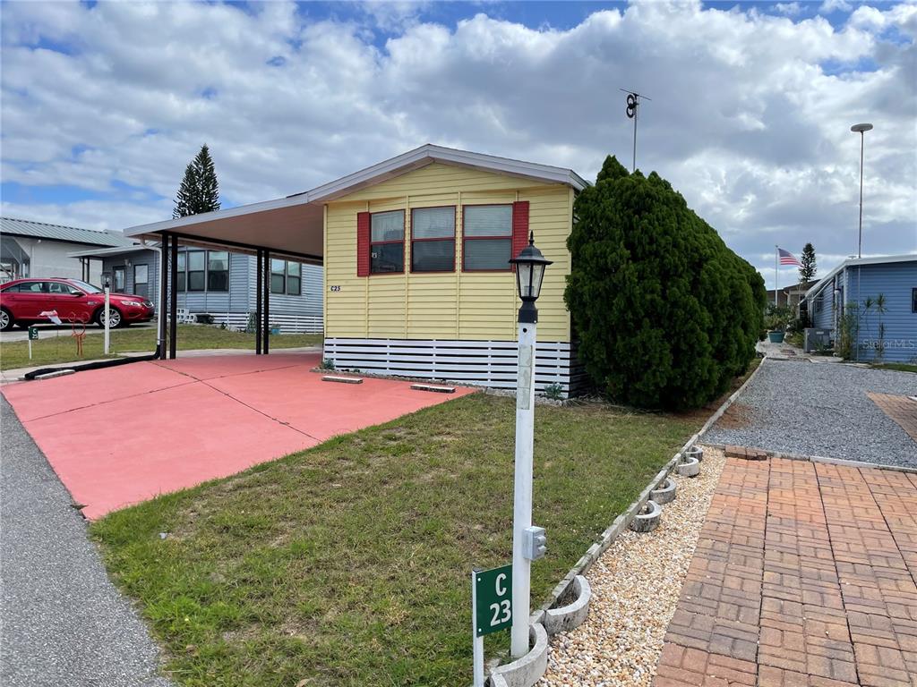 A yellow mobile home features a red concrete driveway, a carport, and a lamp post — 251 PATTERSON ROAD UNIT C25, HAINES CITY, FL