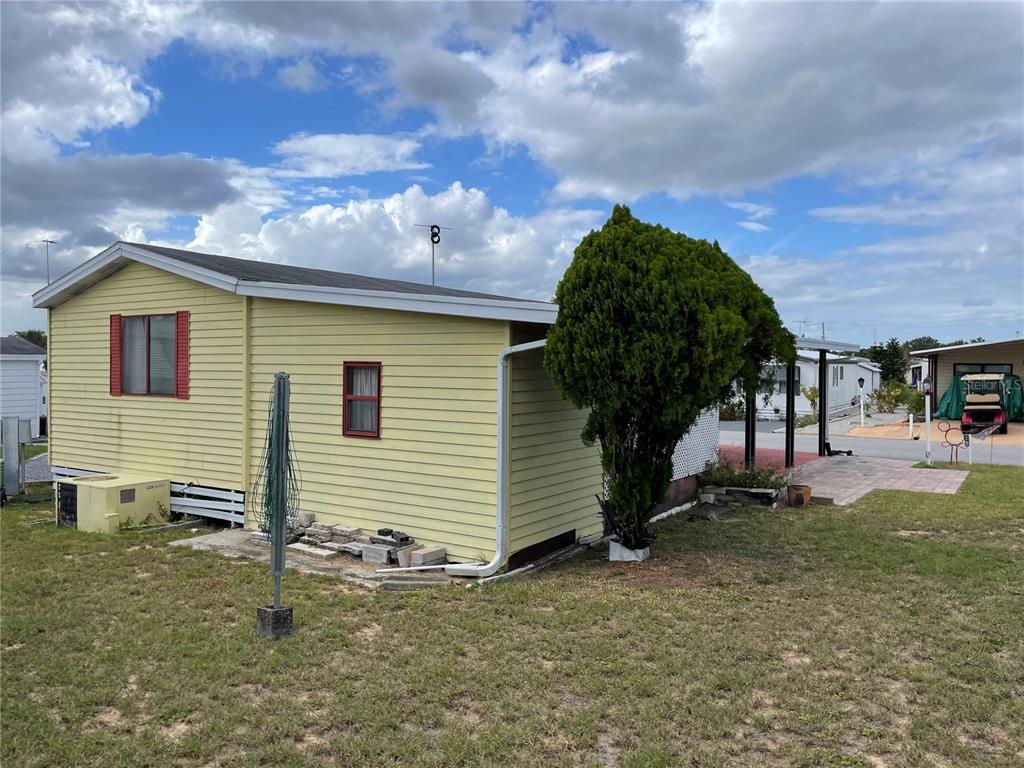 A yellow mobile home with red-trimmed windows and a carport sits on a grassy lot — 251 PATTERSON ROAD UNIT C25, HAINES CITY, FL