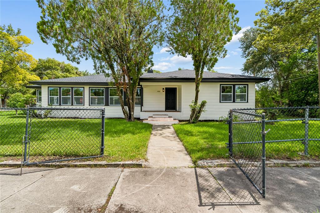 A single-story white house with a black roof and trim sits behind a chain-link fence — 400 PLUMOSA DRIVE, SANFORD, FL