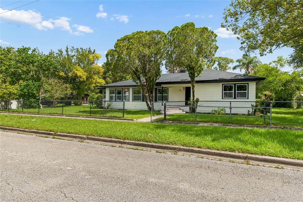 A single-story white house with a dark roof sits behind a chain-link fence — 400 PLUMOSA DRIVE, SANFORD, FL