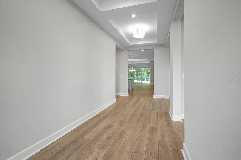 A hallway with light wood flooring leads to an open living area with sliding glass doors — 960 CLUB CRESSWIND DRIVE, LADY LAKE, FL