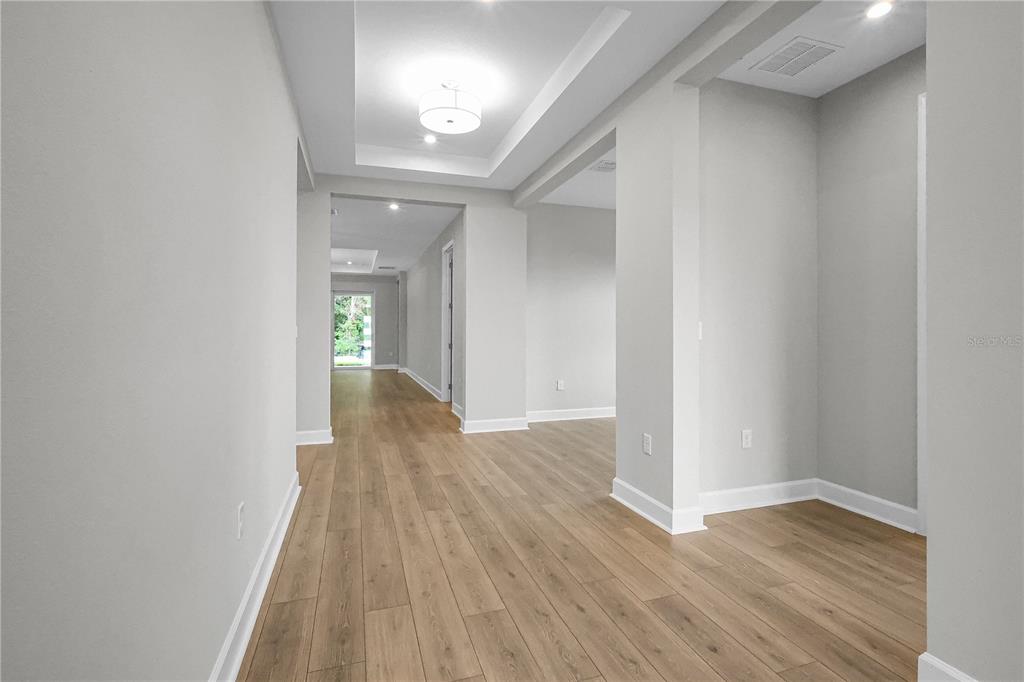 A hallway with light wood flooring leads toward a doorway with a view of greenery — 960 CLUB CRESSWIND DRIVE, LADY LAKE, FL