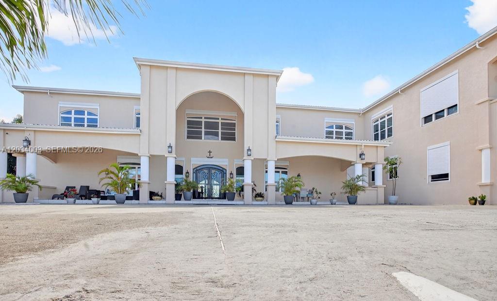 A large, two-story beige house features a prominent arched entryway and a spacious paved courtyard — 15 Paradise View Villa, 00000, FL
