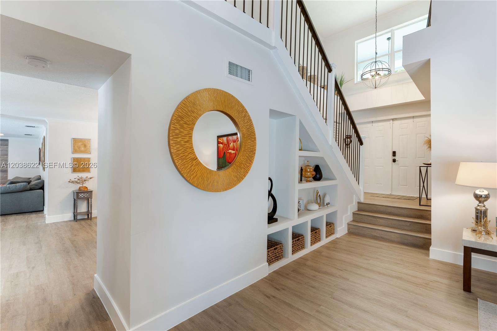 A bright entryway features a staircase with built-in shelving, light wood flooring, and a round mirror — 14830 SW 149th St, Miami FL 33196, MIAMI, FL