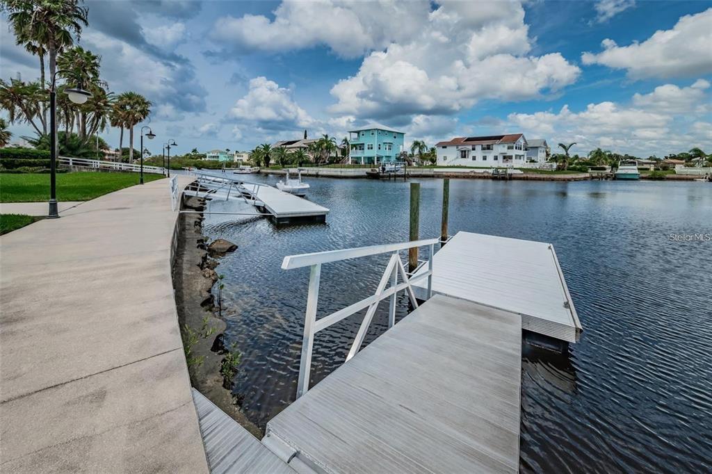 A concrete walkway runs alongside a canal with two floating boat docks and palm trees — 4743 JENNMAR WAY, NEW PORT RICHEY, FL