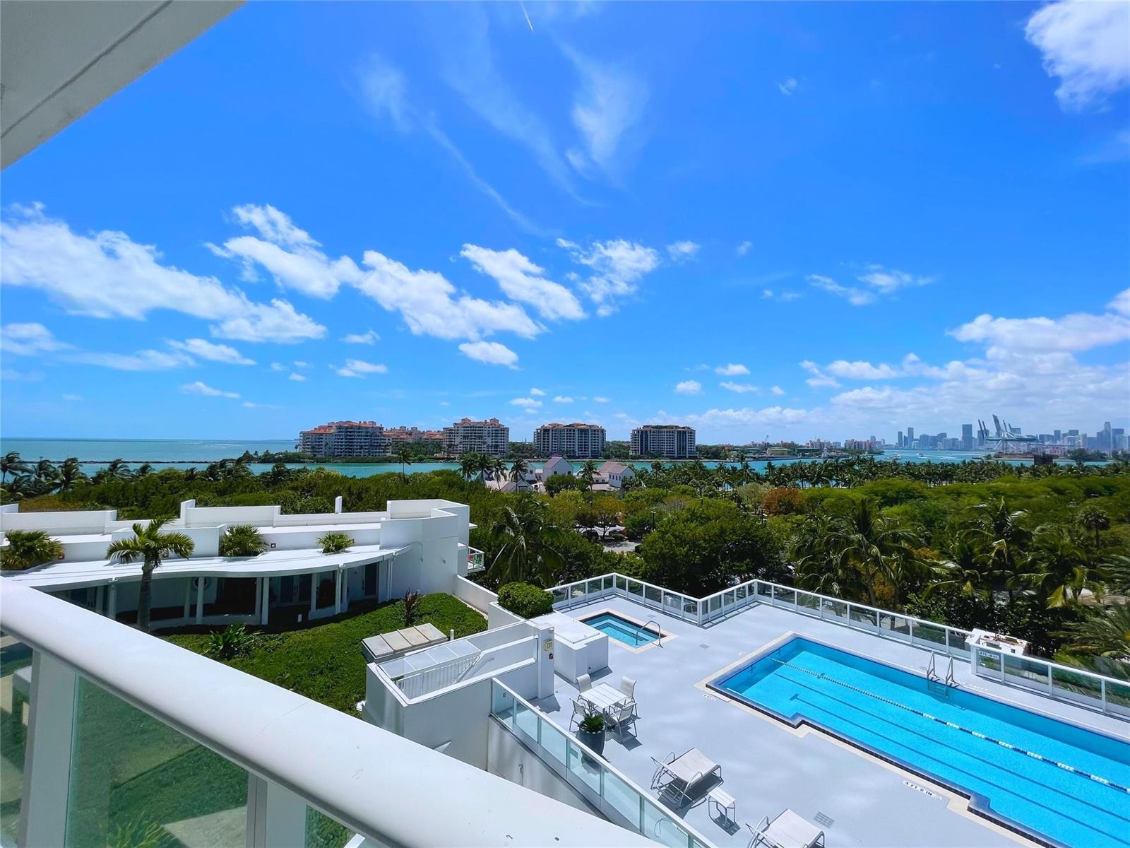 A high-angle view shows a balcony overlooking a swimming pool, lush trees, and the ocean — 100 S Pointe Drive # 602, Miami Beach FL 33139, MIAMI BEACH, FL