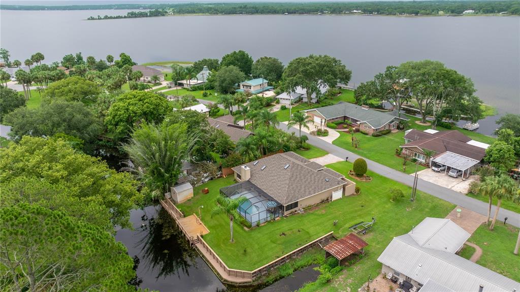An aerial view shows a residential house with a screened pool near a canal and lake — 36 SE CHINICA DRIVE, SUMMERFIELD, FL