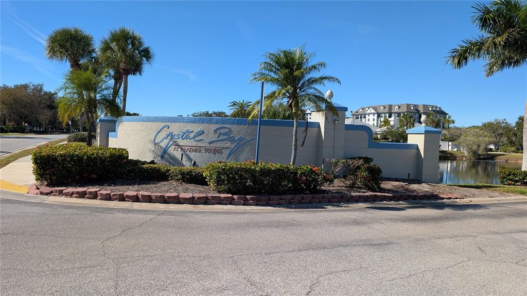 A curved sign for Crystal Bay at Feather Sound sits behind landscaping near a pond — 2333 FEATHER SOUND DRIVE UNIT A208, CLEARWATER, FL