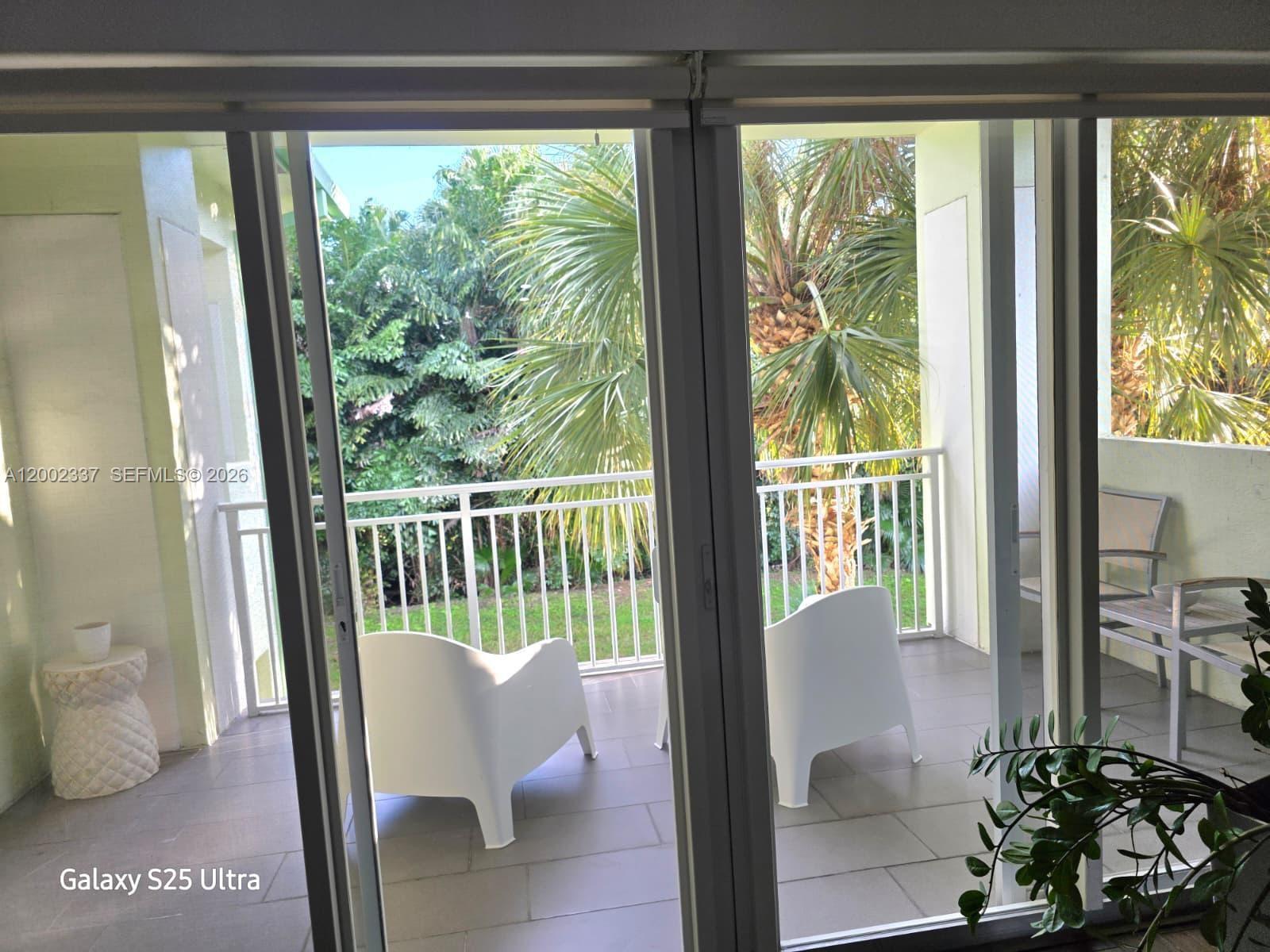 A balcony with white chairs and a small table overlooks lush greenery and palm trees — 5300 NW 87th Ave # 1416, Doral FL 33178, DORAL, FL