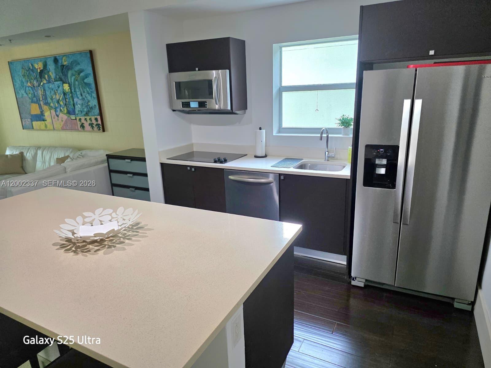 A modern kitchen features dark cabinetry, stainless steel appliances, and a large quartz-topped island — 5300 NW 87th Ave # 1416, Doral FL 33178, DORAL, FL