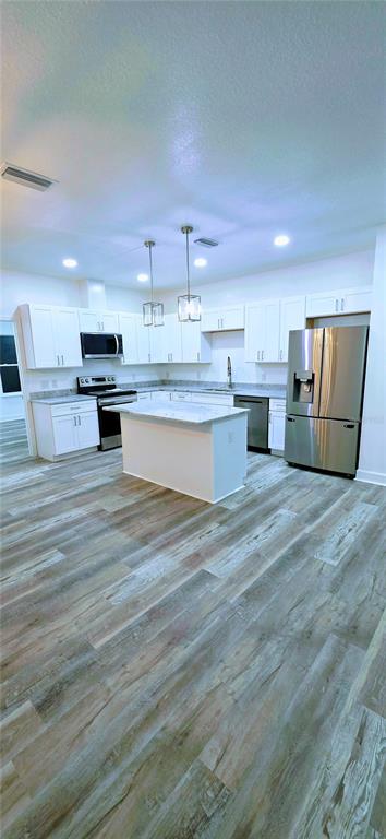 A modern kitchen features white cabinets, stainless steel appliances, a center island, and wood-look flooring — 350 NE 20TH TERRACE, GAINESVILLE, FL