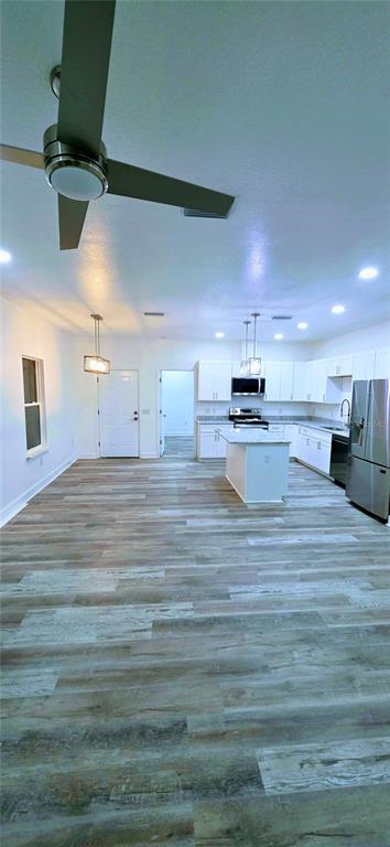 An open-concept kitchen and living area features white cabinetry, a center island, and wood-look flooring — 350 NE 20TH TERRACE, GAINESVILLE, FL