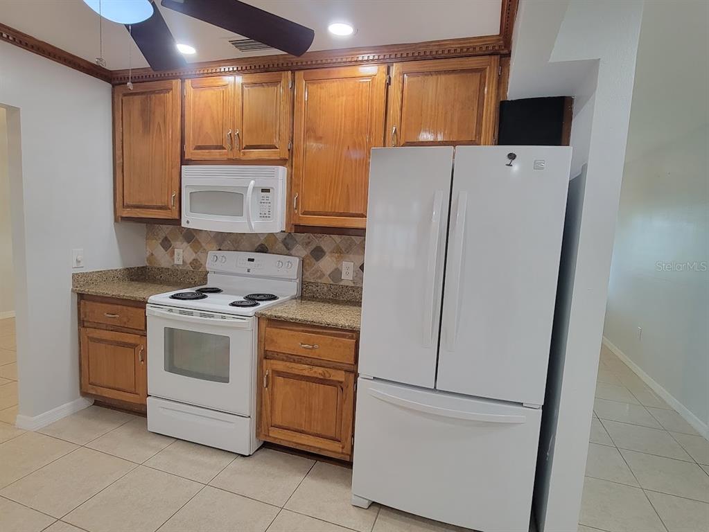 A kitchen features wood cabinets, granite countertops, white appliances, and light-colored tile flooring — 1460 SCHENLEY STREET, PORT CHARLOTTE, FL