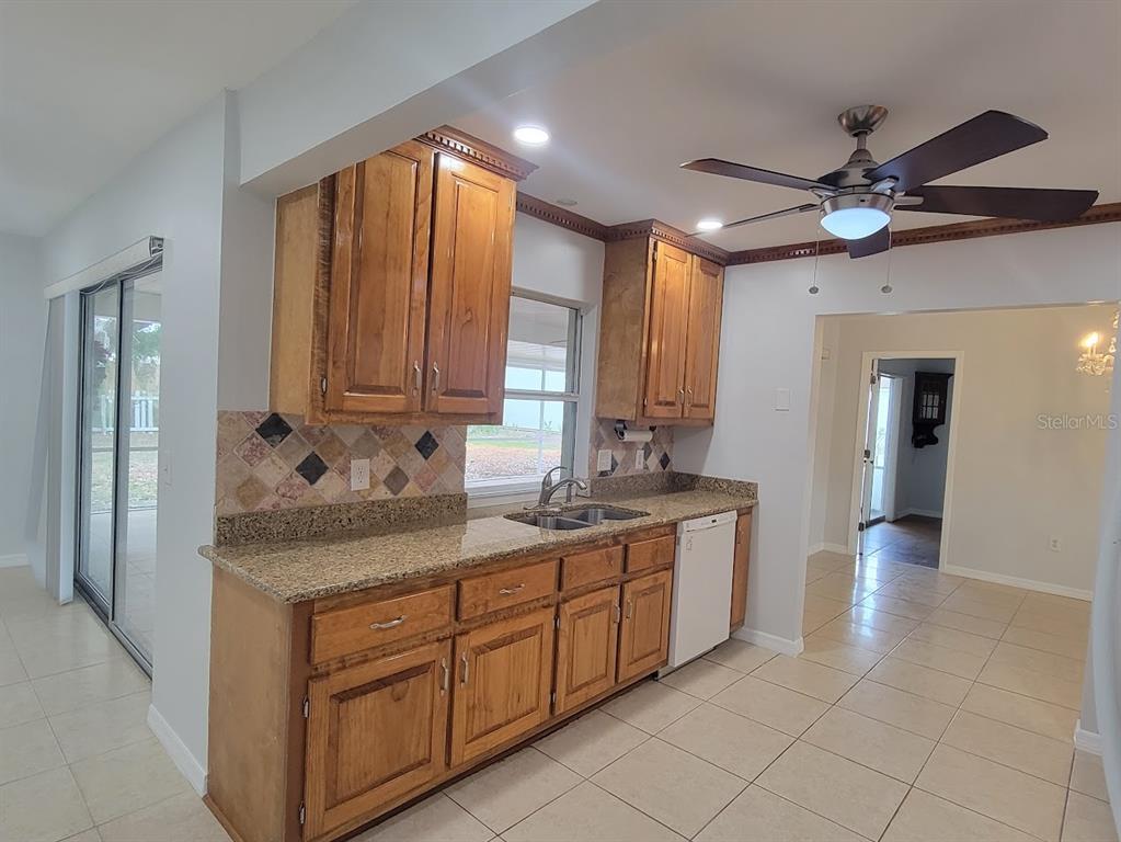 A kitchen features wood cabinets, granite countertops, a tile backsplash, and a ceiling fan — 1460 SCHENLEY STREET, PORT CHARLOTTE, FL