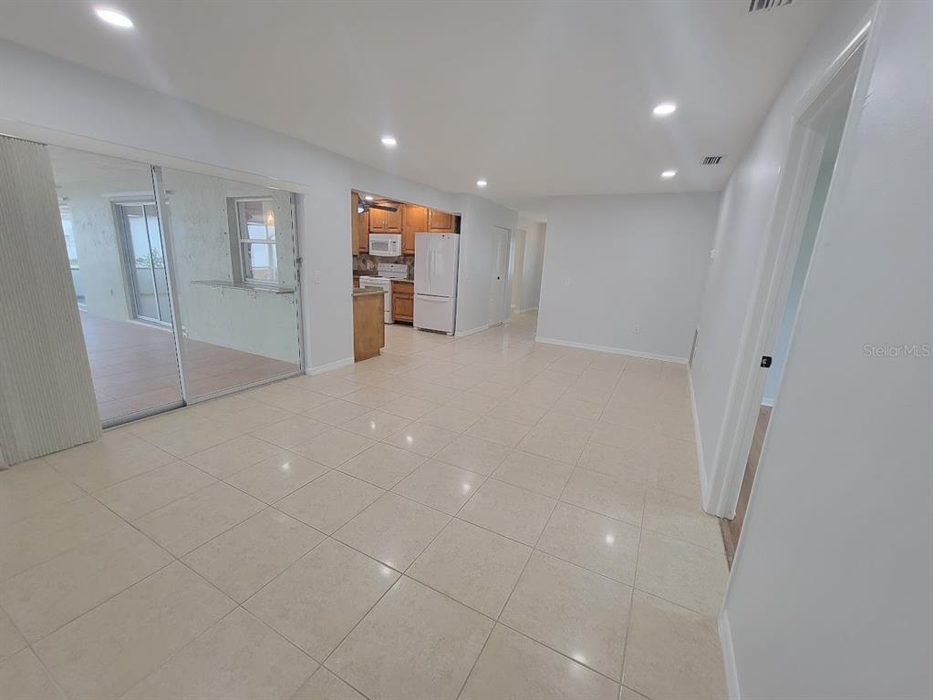 A bright, open-concept living area features light-colored tile flooring, recessed lighting, and a kitchen view — 1460 SCHENLEY STREET, PORT CHARLOTTE, FL