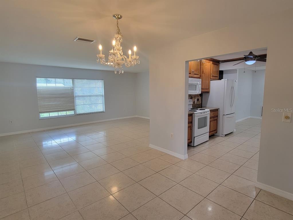 A dining area with a chandelier and tile floors opens into a kitchen with cabinets — 1460 SCHENLEY STREET, PORT CHARLOTTE, FL