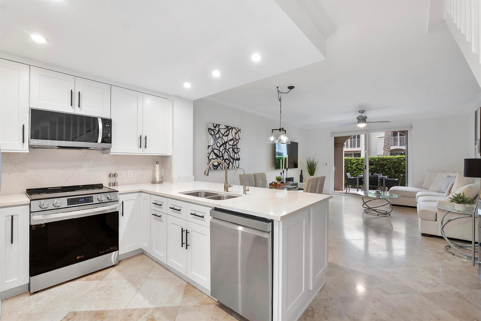 A modern kitchen with white cabinets and stainless steel appliances opens to a living area — 3596 S Ocean Boulevard # 102, Highland Beach FL 33487, HIGHLAND BEACH, FL