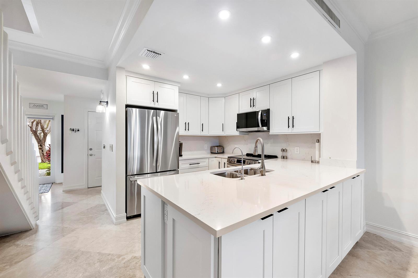 A modern white kitchen features stainless steel appliances, a large island, and light stone countertops — 3596 S Ocean Boulevard # 102, Highland Beach FL 33487, HIGHLAND BEACH, FL