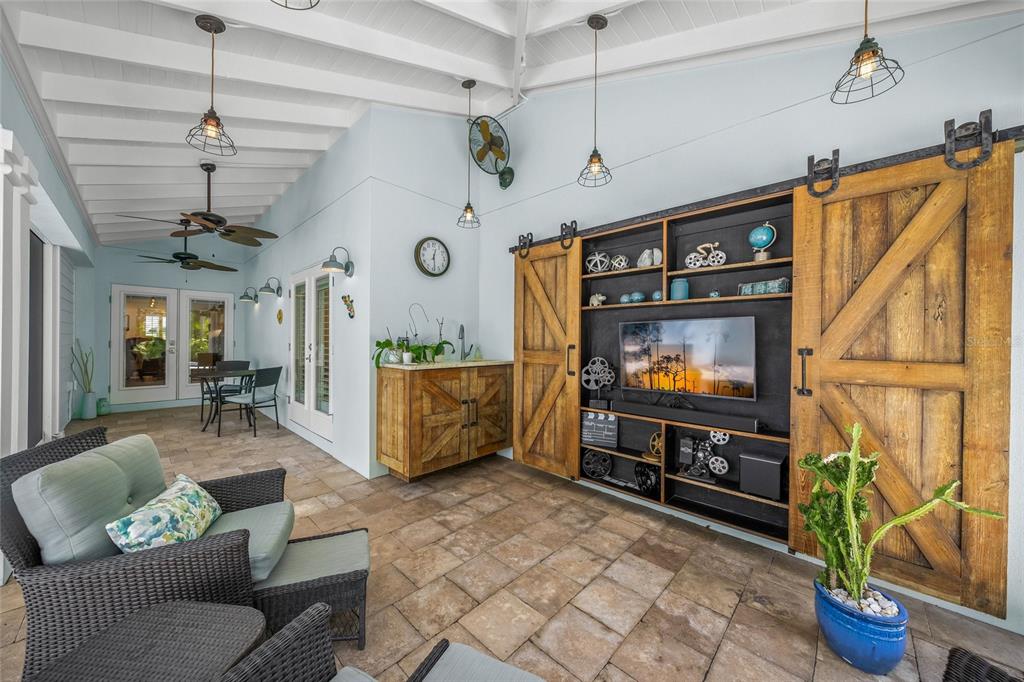 A covered patio features a television entertainment center with sliding barn doors and wicker furniture — 2440 ARLINGTON STREET, SARASOTA, FL