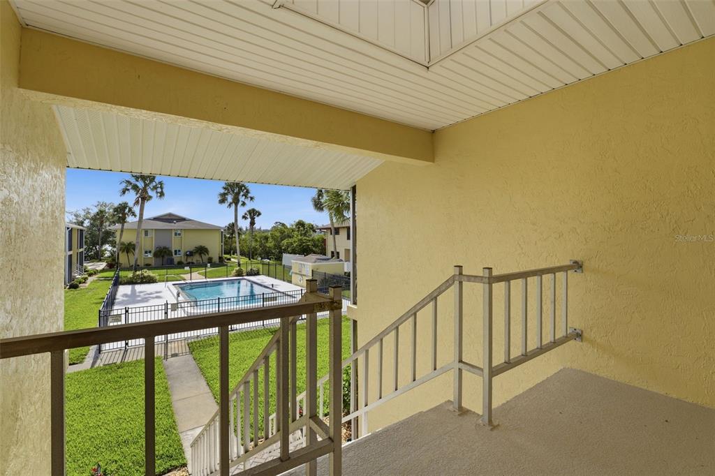 An outdoor stairwell with metal railings overlooks a swimming pool and a neighboring apartment building — 101 LOUELLA LANE UNIT 2, NOKOMIS, FL