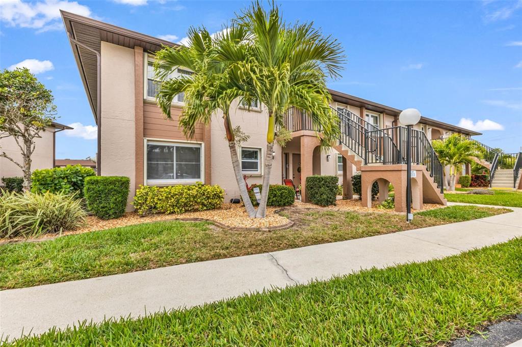 A two-story apartment building exterior features tan stucco walls, a palm tree, and outdoor stairs — 25100 SANDHILL BOULEVARD UNIT 201, PUNTA GORDA, FL