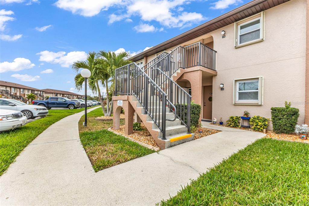 An exterior view of a two-story apartment building with an outdoor staircase and palm trees — 25100 SANDHILL BOULEVARD UNIT 201, PUNTA GORDA, FL