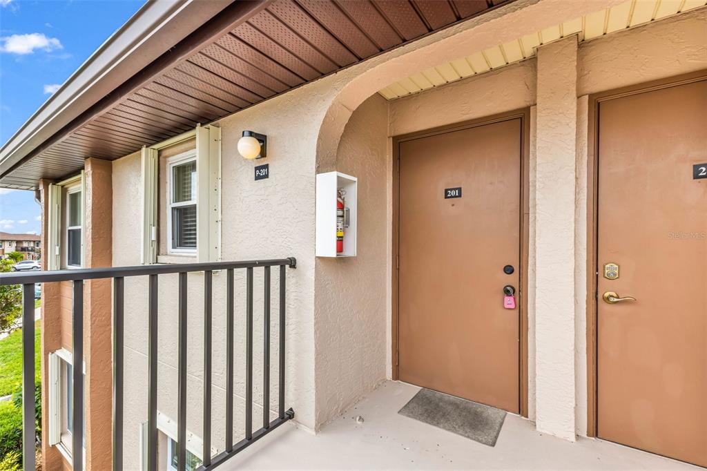 An exterior view of a second-floor apartment balcony with two brown entry doors — 25100 SANDHILL BOULEVARD UNIT 201, PUNTA GORDA, FL