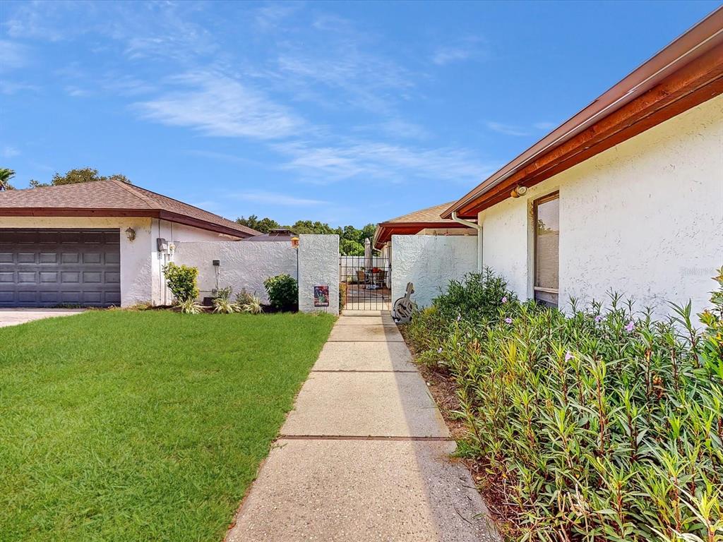 A concrete walkway leads between two white stucco buildings toward a metal gate — 111 TUXFORD DRIVE, HAINES CITY, FL