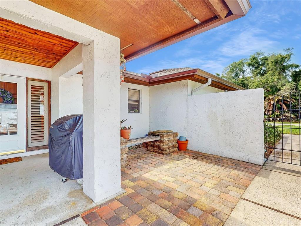 A covered patio features a brick paver floor, a stone bench, and a covered grill — 111 TUXFORD DRIVE, HAINES CITY, FL