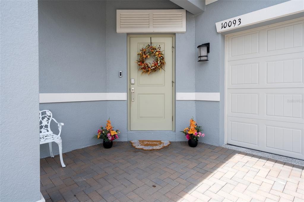 A light blue house exterior features a pale green front door, a white chair, and pavers — 10093 CAMPANULA COURT, LAND O LAKES, FL