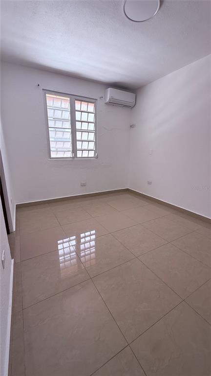 An empty room with beige tile flooring, white walls, a window, and a wall-mounted air conditioner — 413 EDIFICIO GAITHER PLAZA APT. 3A, SAN JUAN, PR