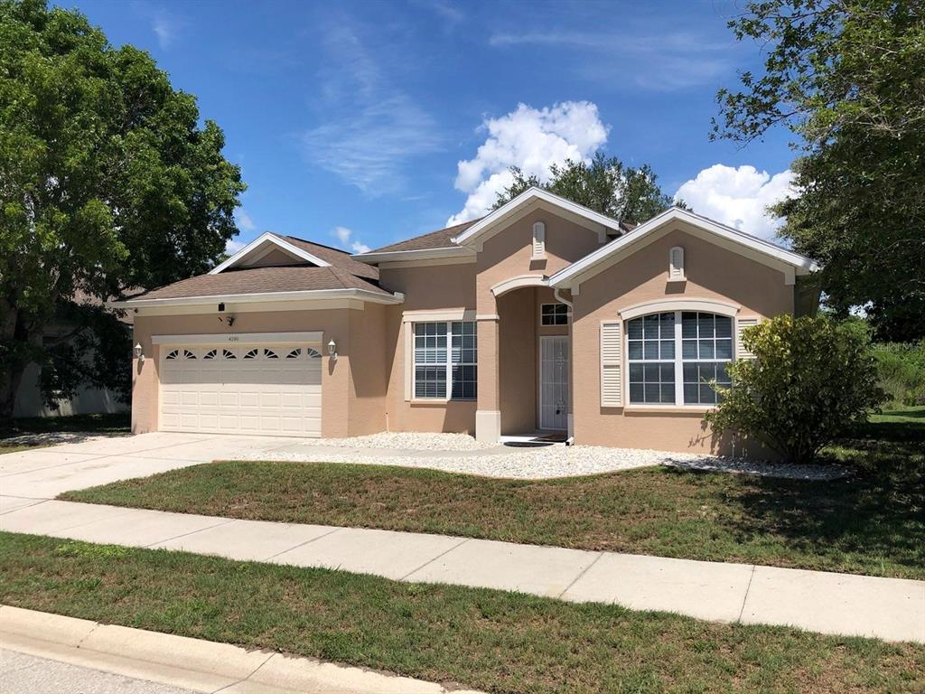 A single-story tan house with a two-car garage, white trim, and a landscaped front yard — 4200 TENNYSON WAY, VENICE, FL