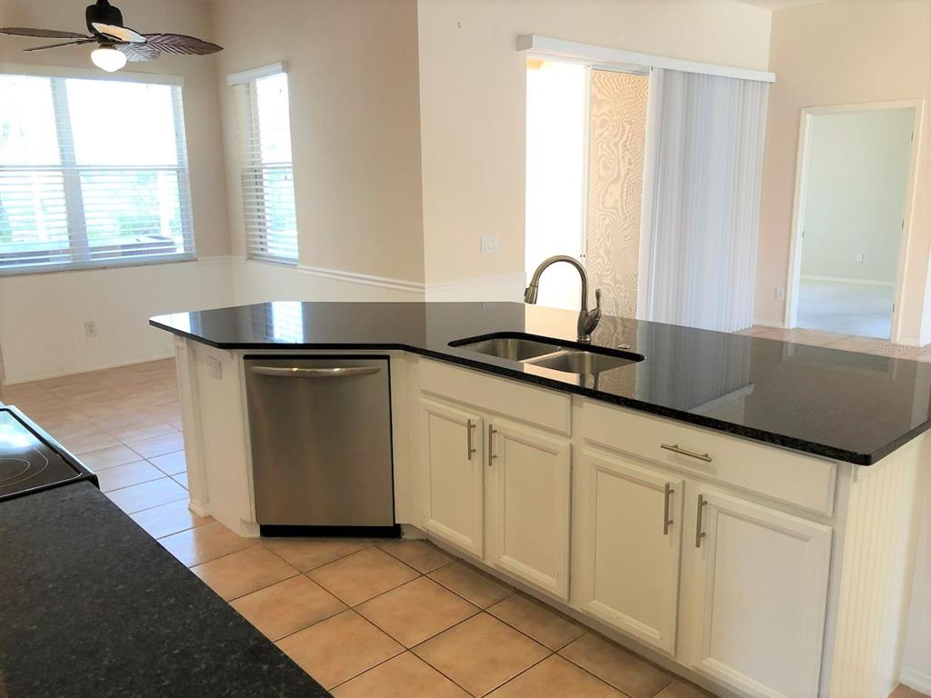 A kitchen island with a black countertop, stainless steel dishwasher, and white cabinets — 4200 TENNYSON WAY, VENICE, FL