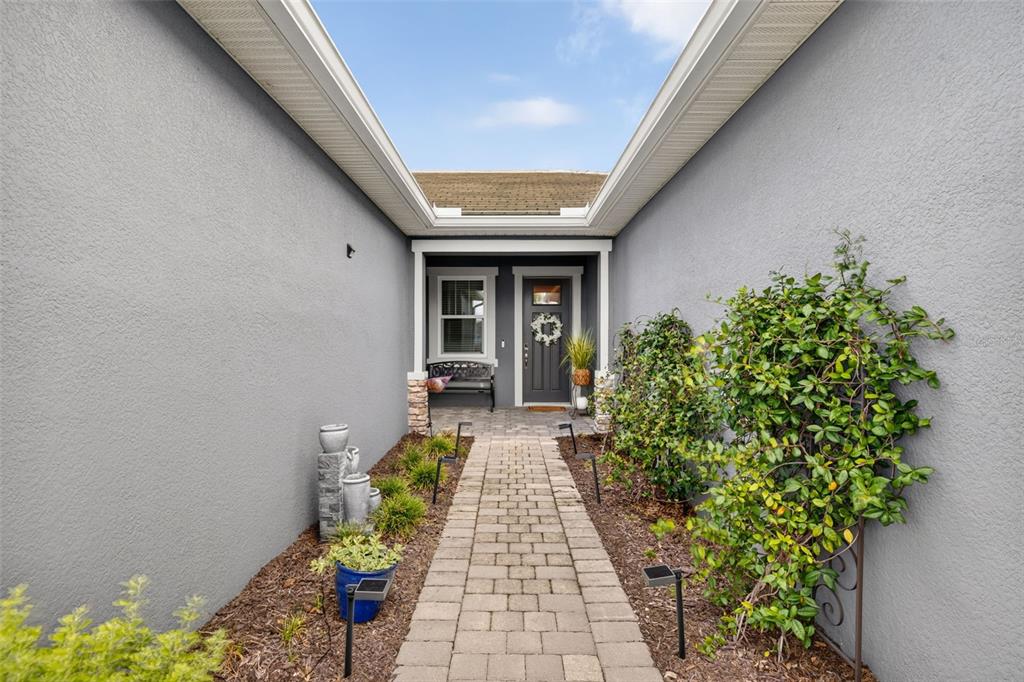 A paved walkway leads to a gray front door framed by stucco walls and landscaping — 12550 SOMATIC COURT, VENICE, FL