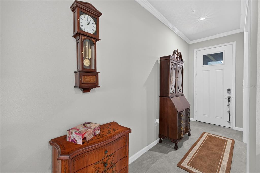 An entryway features a wall-mounted clock, a wooden cabinet, and a desk near a white door — 12550 SOMATIC COURT, VENICE, FL