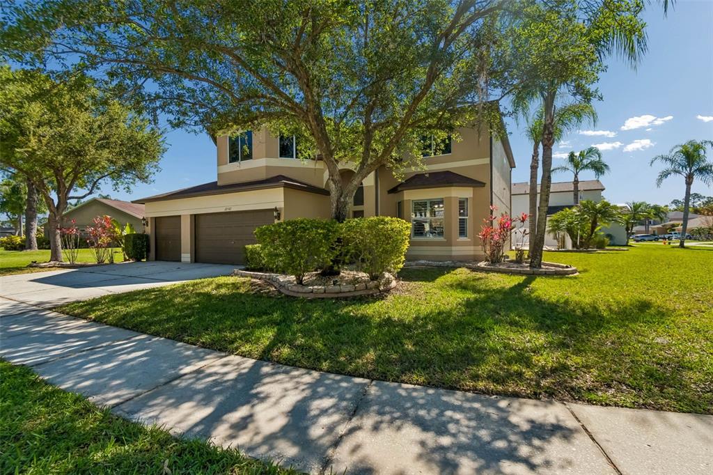 A two-story suburban house with a tan exterior, a two-car garage, and a large tree — 12507 ASHDOWN DRIVE, ODESSA, FL