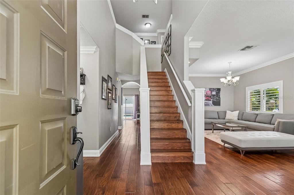 An entryway features hardwood floors, a wooden staircase, and a view into a living room — 12507 ASHDOWN DRIVE, ODESSA, FL