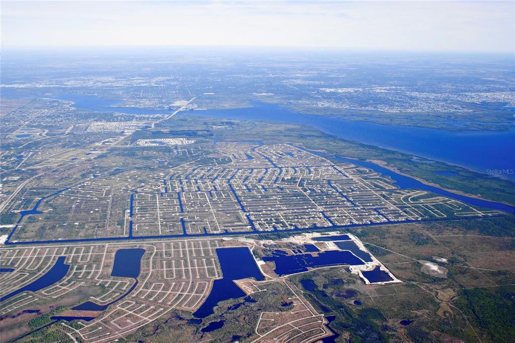 An aerial view shows a residential development with canal-lined streets and nearby bodies of water — 9314 HARVESTER STREET, PORT CHARLOTTE, FL