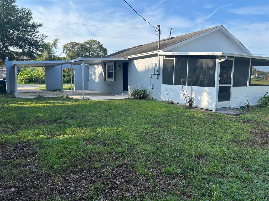 A single-story house features a side carport, a screened-in porch, and a grassy yard — 1450 AGATHA DRIVE, DELTONA, FL