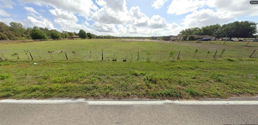 A wide, grassy, fenced-in vacant lot viewed from a paved road under a cloudy sky — SWEET HILL RD, POLK CITY, FL