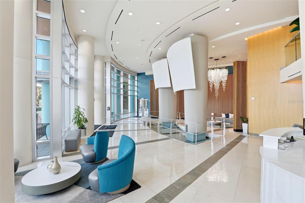 A modern lobby features blue armchairs, white tile floors, floor-to-ceiling windows, and a crystal chandelier — 322 E CENTRAL BOULEVARD UNIT 1109, ORLANDO, FL