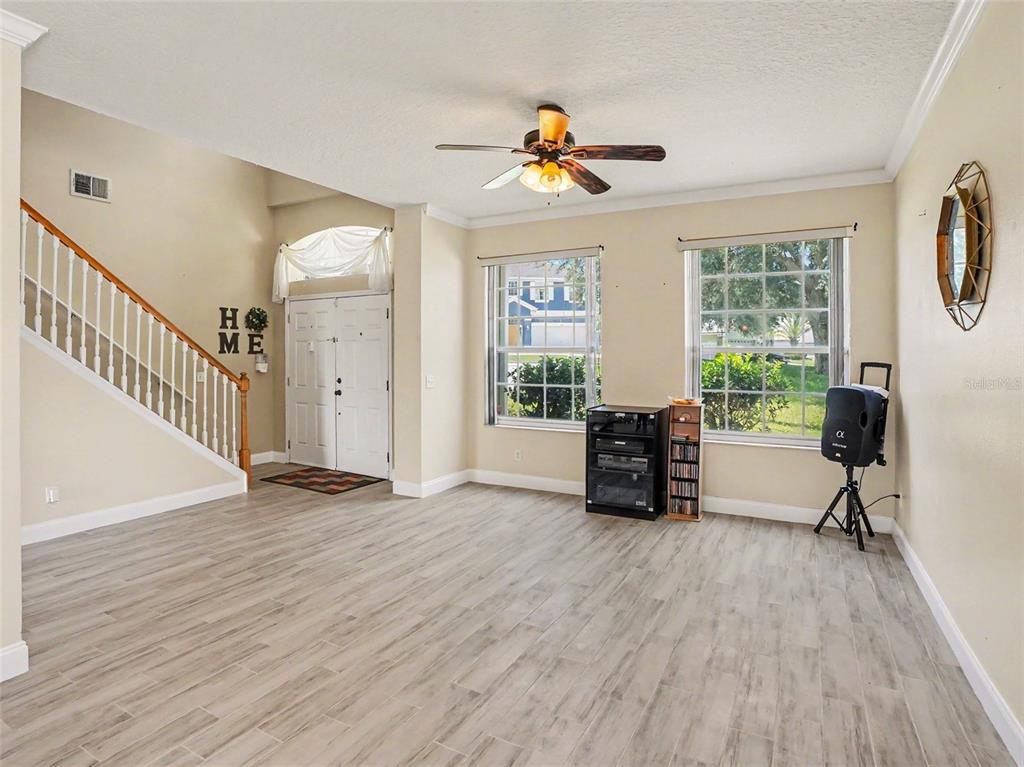 A living room with light wood-look tile flooring, a staircase, and two large windows — 1602 PRESIDIO DRIVE, CLERMONT, FL