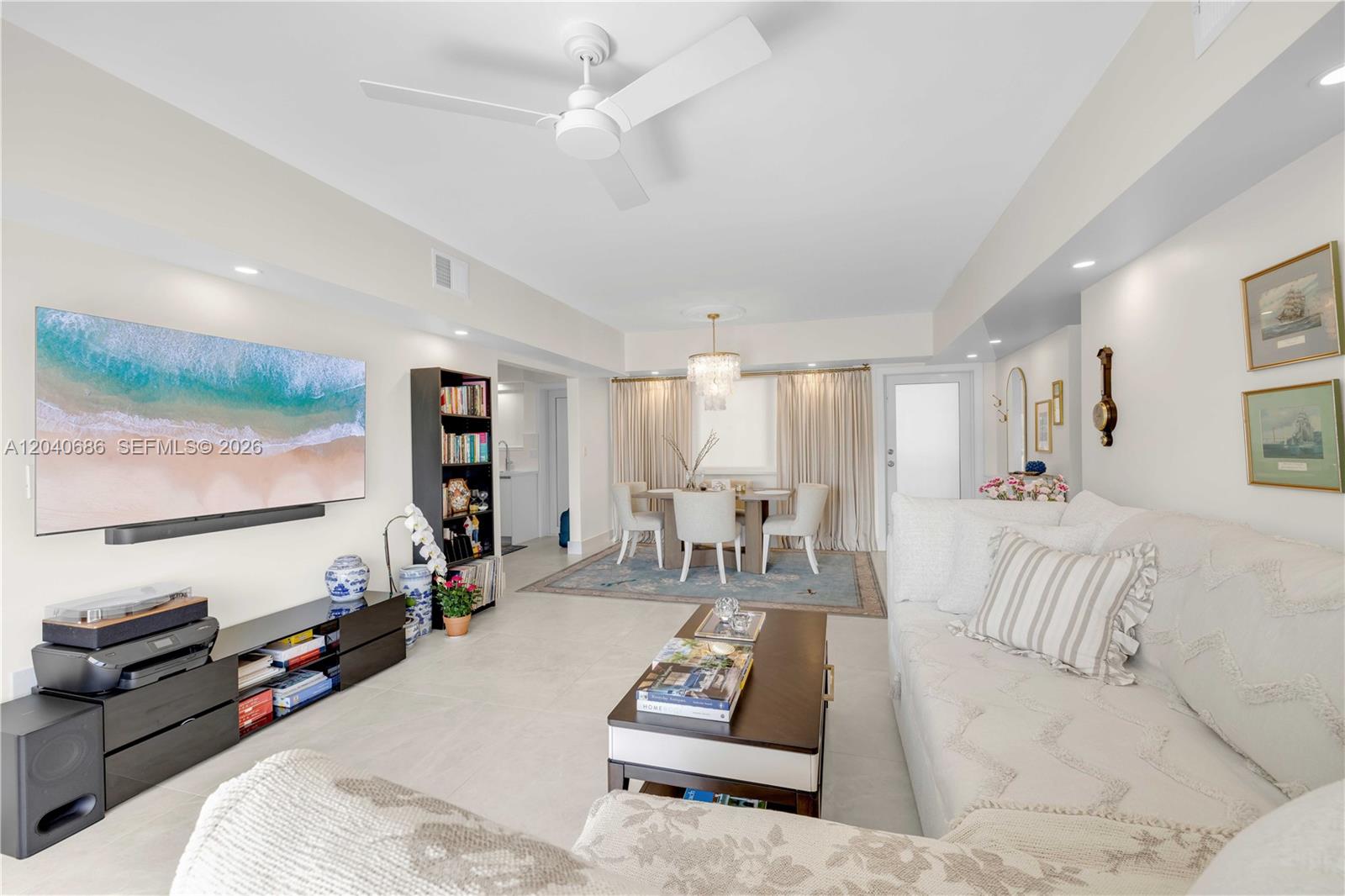 A bright living and dining area features white tile floors, a ceiling fan, and furniture — 462 Golden Isles Dr # 211, Hallandale Beach FL 33009, HALLANDALE BEACH, FL
