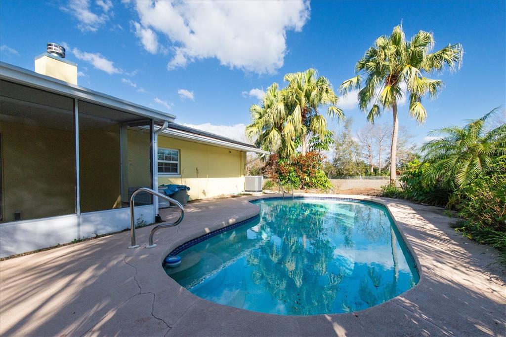 A backyard swimming pool sits next to a yellow house with a screened-in porch — 13400 91ST AVENUE, SEMINOLE, FL