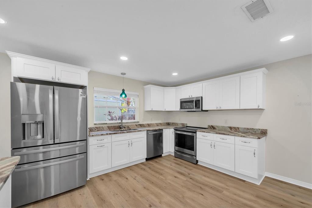 A kitchen features white cabinets, stainless steel appliances, wood-look flooring, and stone countertops — 13400 91ST AVENUE, SEMINOLE, FL
