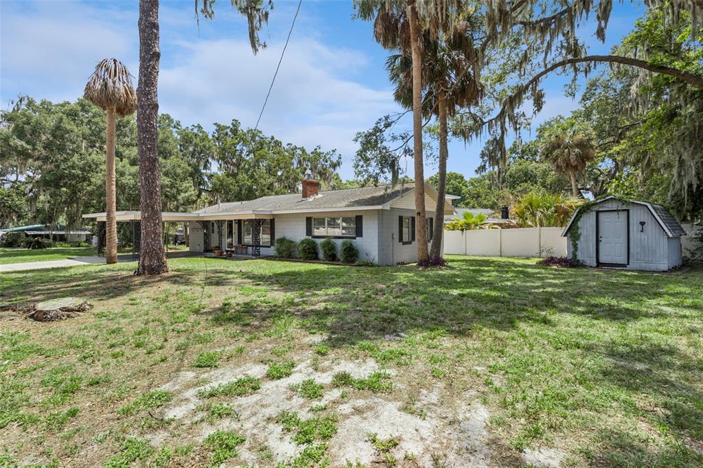 A single-story gray house with a carport and a detached shed in a grassy yard — 1400 SPARTAN AVENUE, LEESBURG, FL