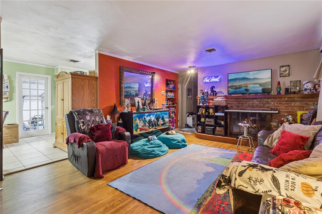 A living room features a brick fireplace, a rainbow rug, and an orange accent wall — 1400 SPARTAN AVENUE, LEESBURG, FL