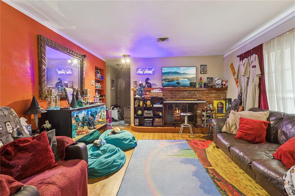 A living room features a brick fireplace, a television, beanbag chairs, and eclectic pop-culture decor — 1400 SPARTAN AVENUE, LEESBURG, FL