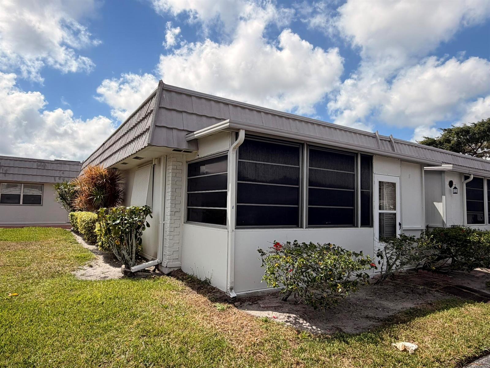Exterior view of a single-story home with a screened-in porch and a metal roof — 43 Valencia B, Delray Beach FL 33446, DELRAY BEACH, FL
