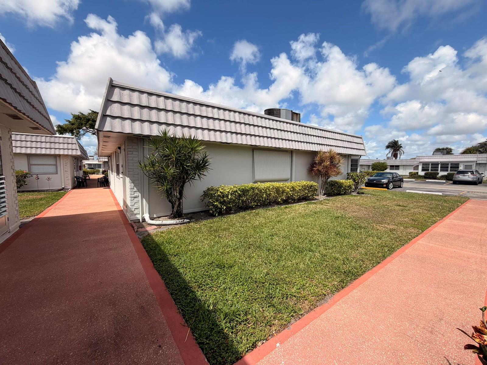 A low-rise residential building with a tiled roof, lawn, and red walkways under a sky — 43 Valencia B, Delray Beach FL 33446, DELRAY BEACH, FL